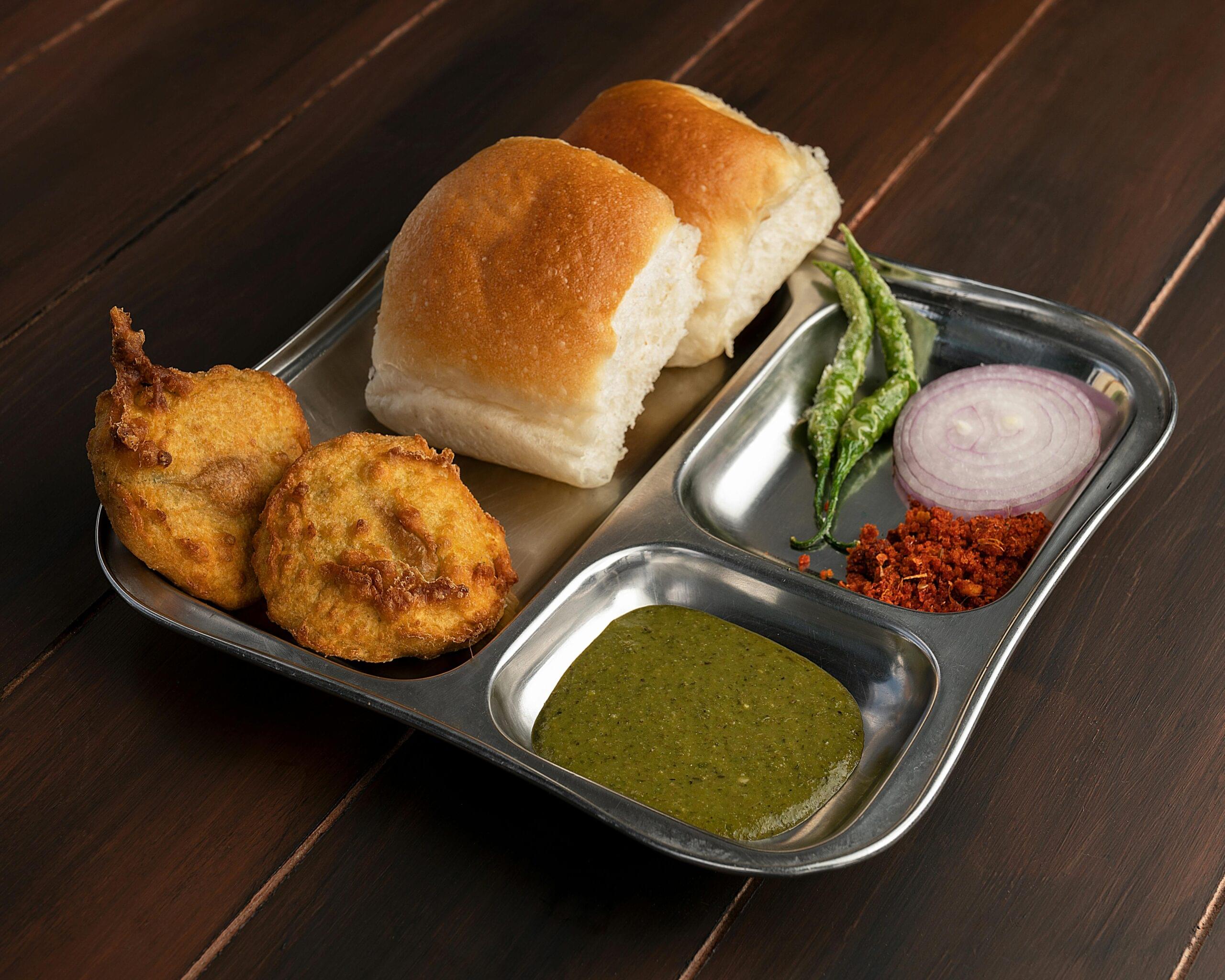 Delicious Maharashtrian Vada Pav served with chutney and spices on a stainless steel plate.